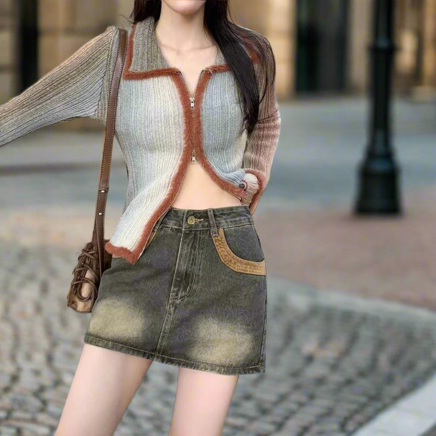 Woman wearing a patterned cardigan, light-colored top, and denim skirt on a tiled pavement.