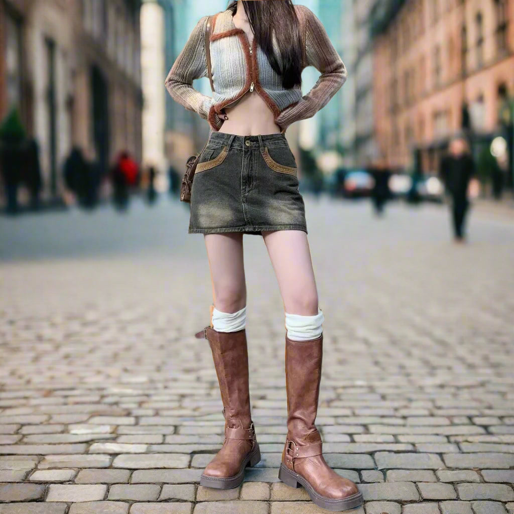 Person wearing a sheer top, denim skirt, and brown knee-high boots on a city street.
