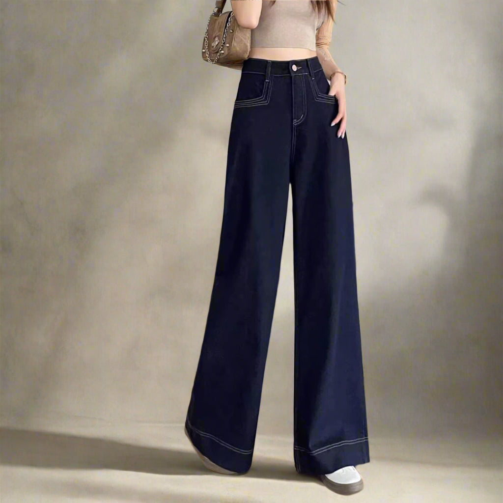 Person wearing dark blue jeans standing in front of the wall.