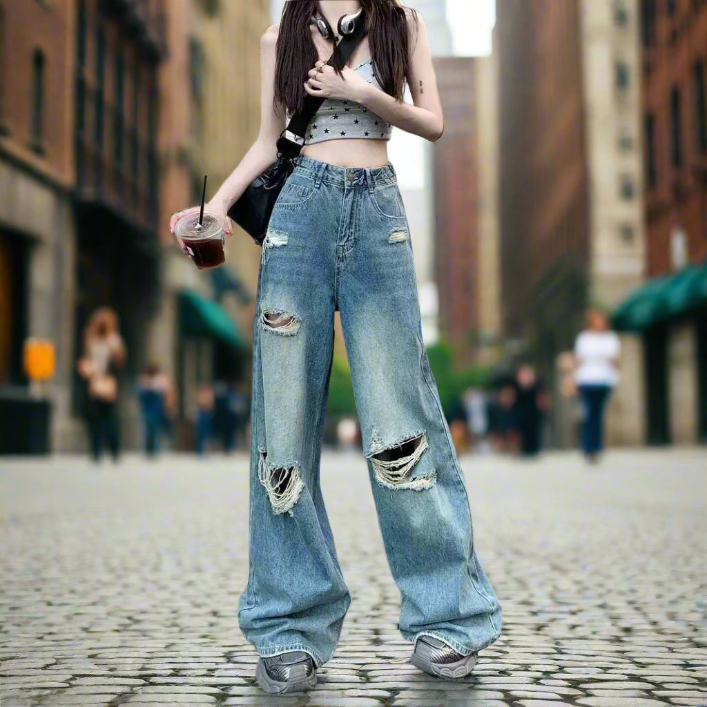 Person wearing ripped blue jeans and a crop top, standing on a street.