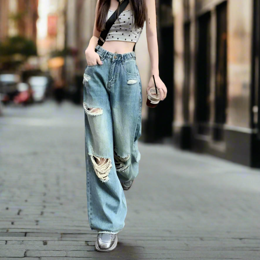 Woman wearing a patterned top and ripped jeans standing on a street.