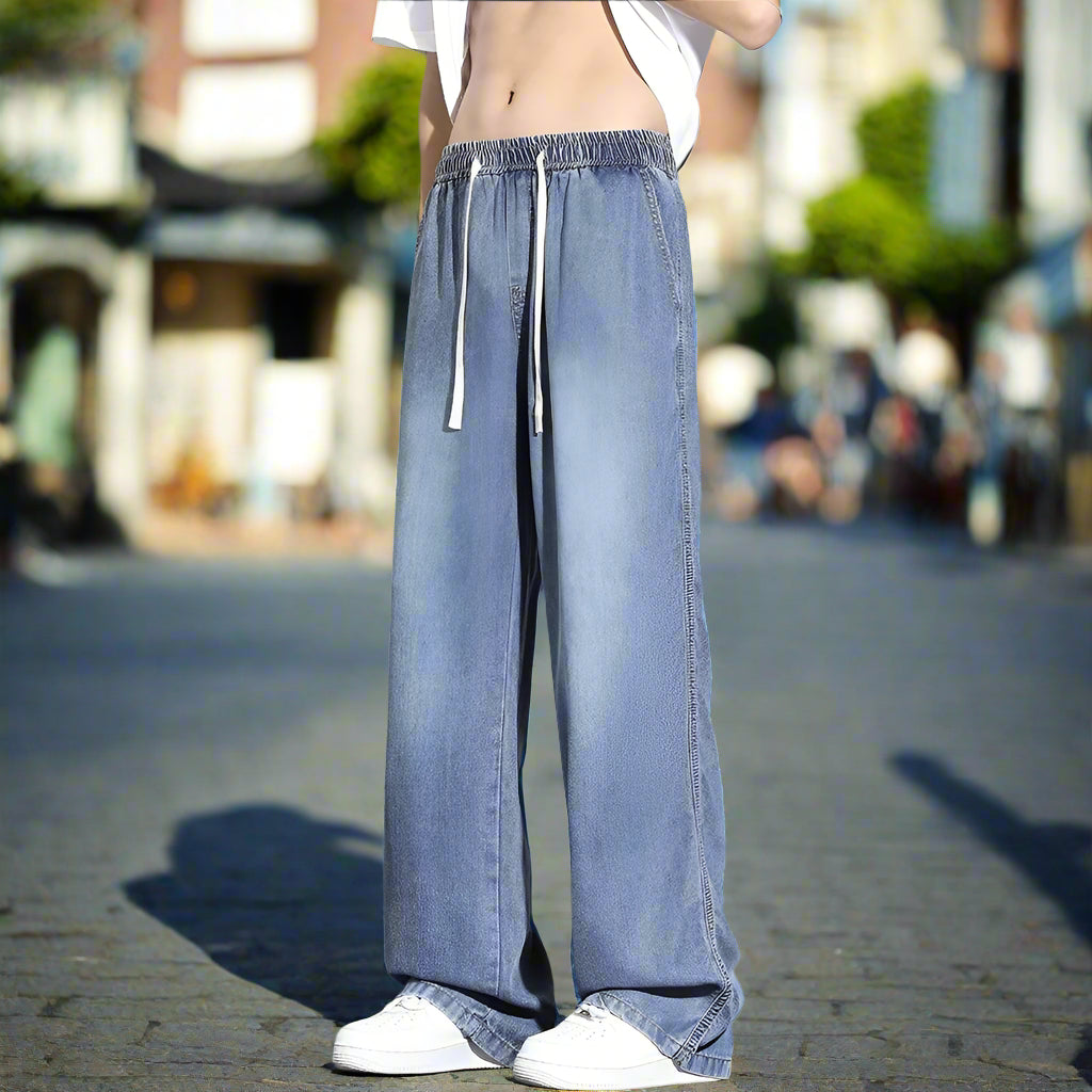Wide-leg blue jeans worn by a person on a gray background