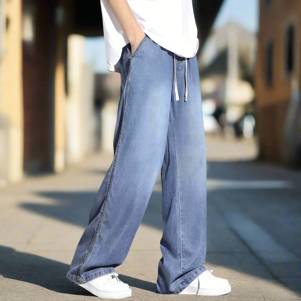 Person wearing wide-leg blue jeans and white sneakers on a gray background