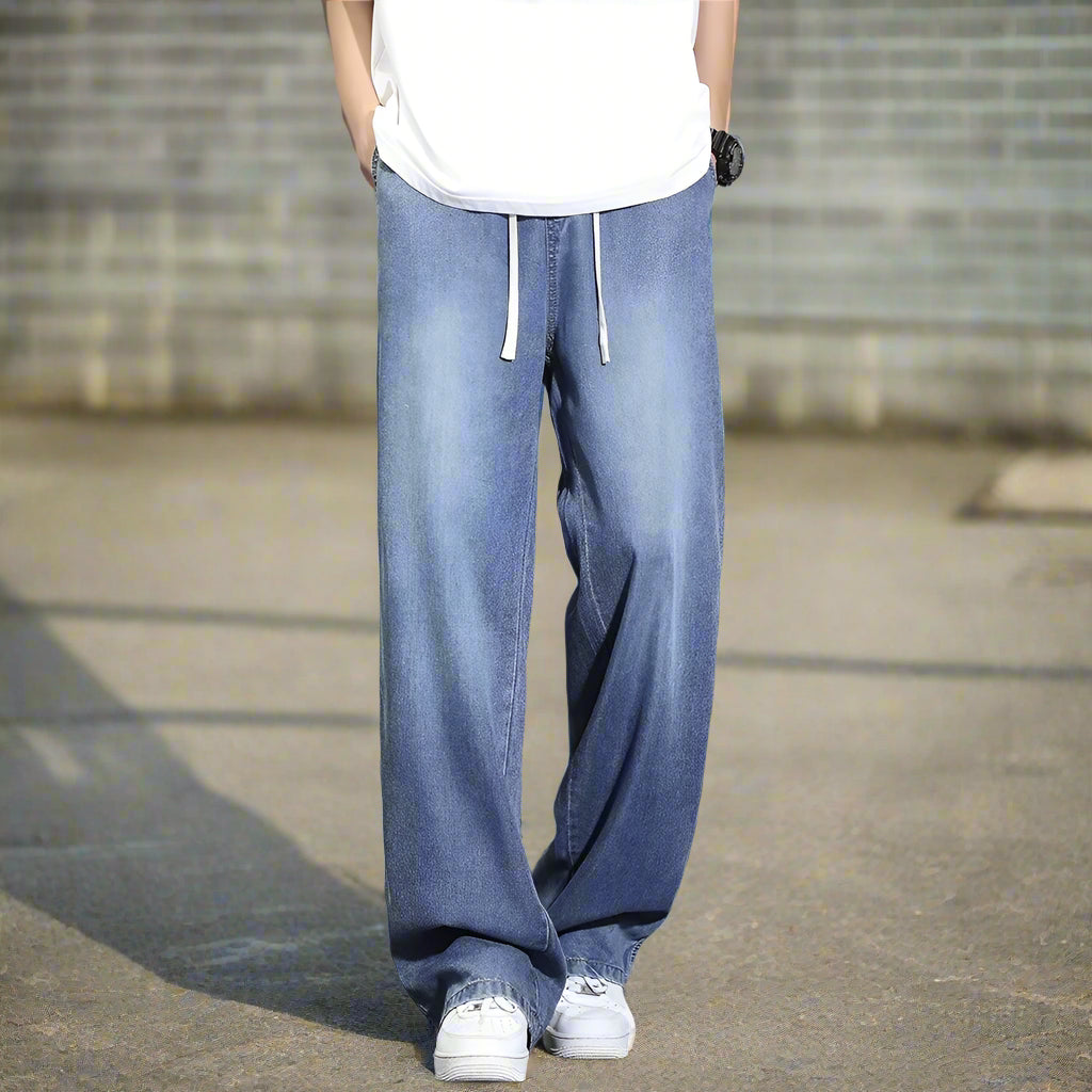Person wearing light blue jeans and white sneakers on a gray background